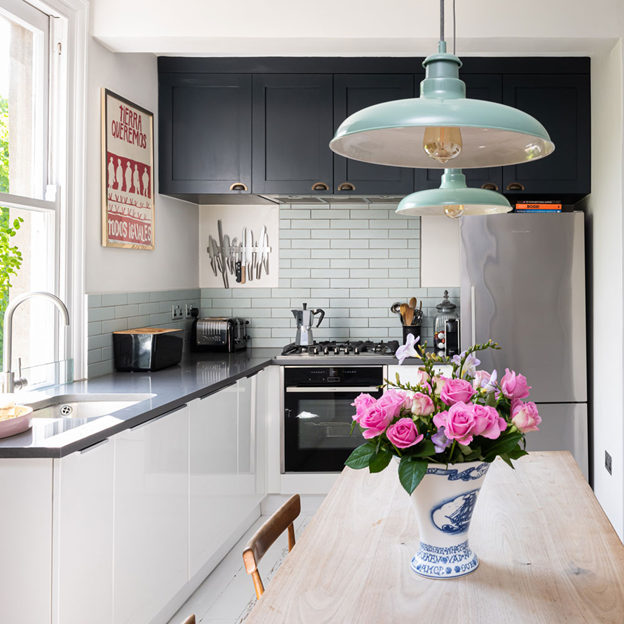 Nhà bếp hình chữ L với tủ đen và trắng, đèn mặt dây chuyền màu xanh lam và bình hoa hồng hồng